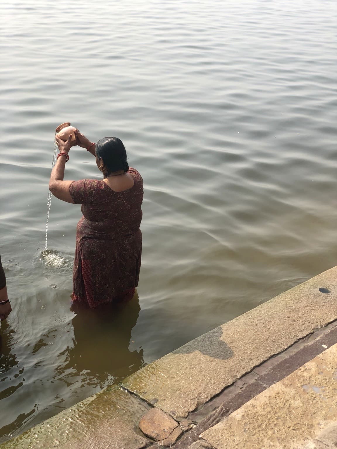 A woman stands in the Ganges and pours water from a small vessel in Varanasi, 2019