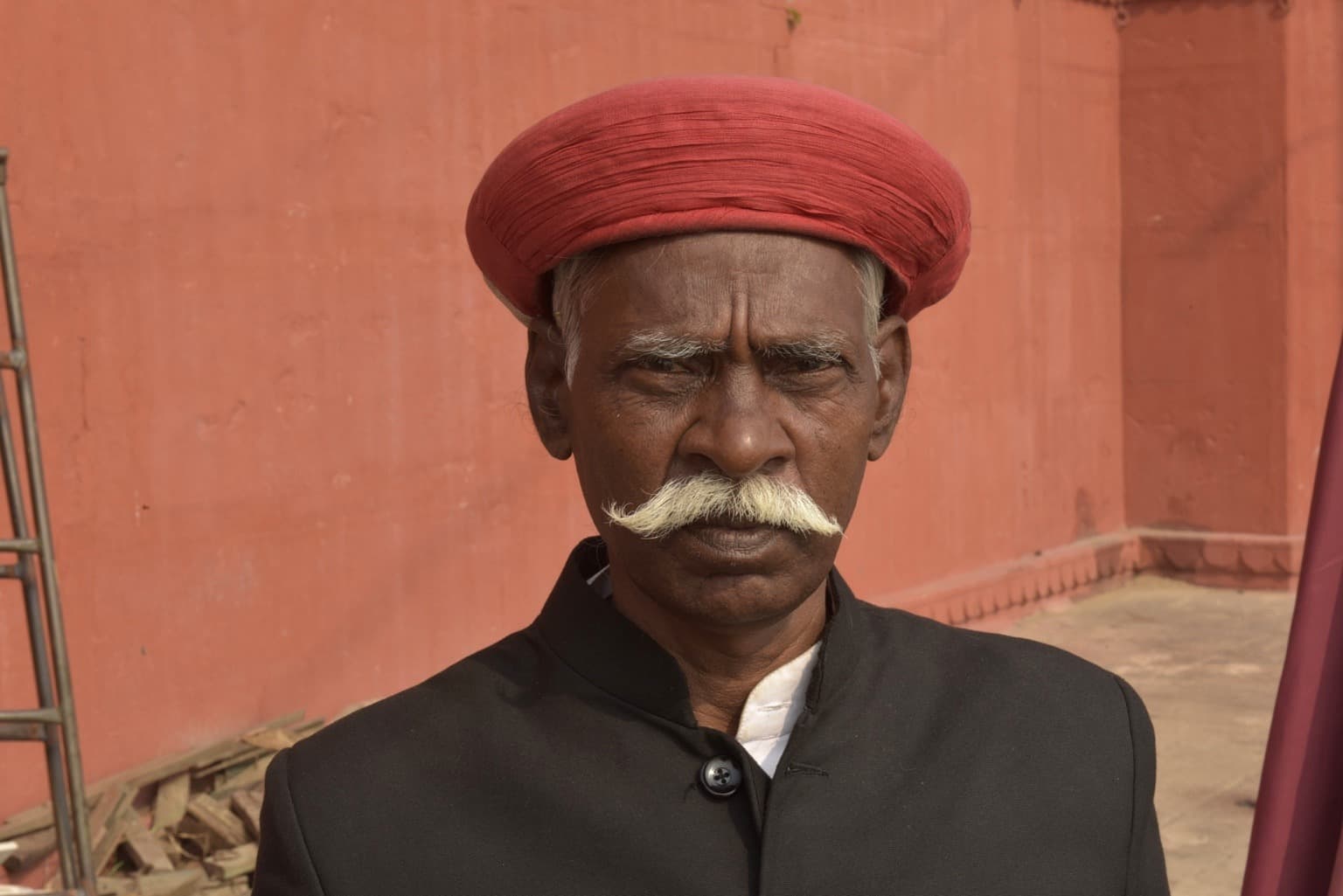 A man wearing a red turban and black coat looks toward the camera in Varanasi, 2019