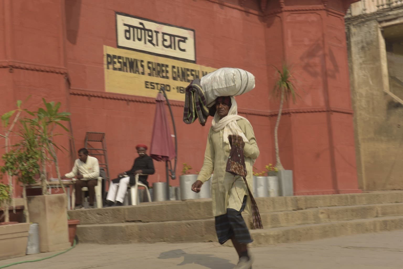 A man walks along the ghats carrying a bundled load on his head, Varanasi, 2019