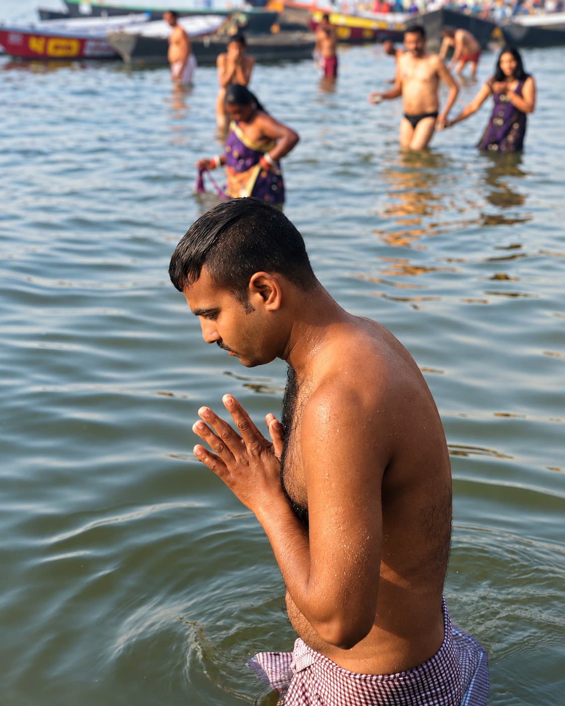 A man stands waist-deep in the Ganges with palms pressed together in prayer, Varanasi, 2019