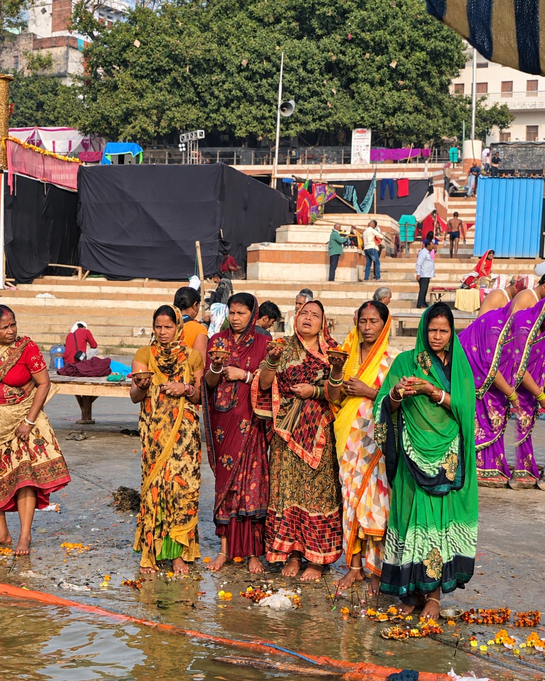 A group of women stands together at the riverfront holding small offerings in Varanasi, 2019