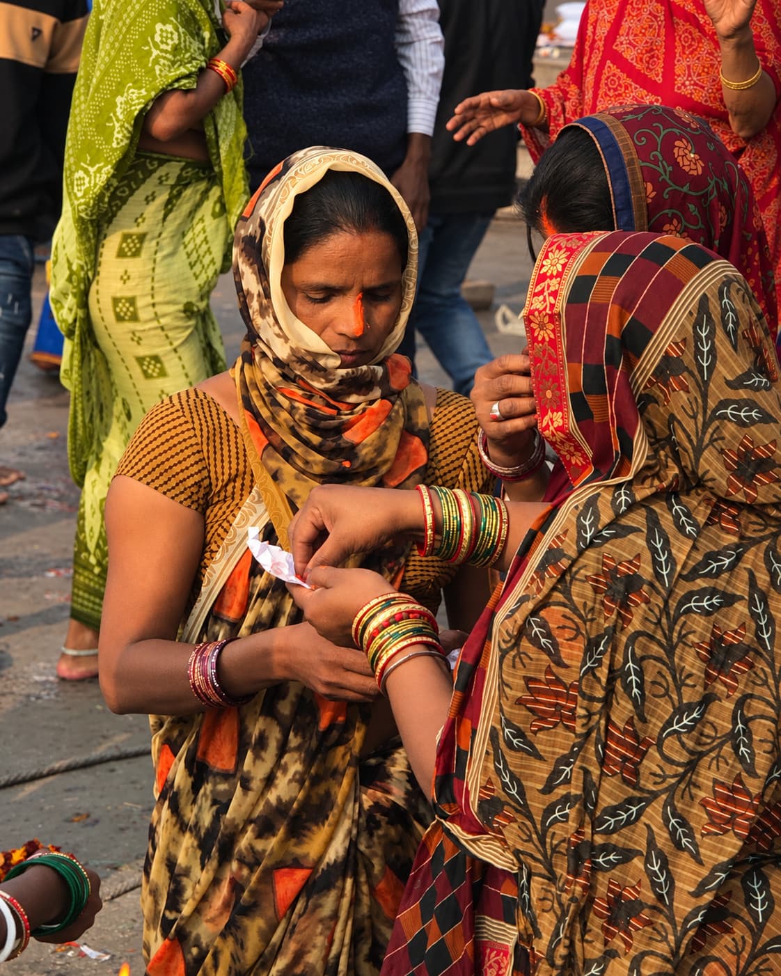 Two women stand close together during a riverfront ritual as one holds folded paper and the other reaches toward it in Varanasi, 2019