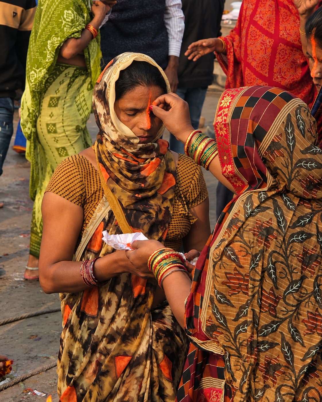 One woman applies a vivid orange mark to another woman’s forehead during a riverfront ritual in Varanasi, 2019