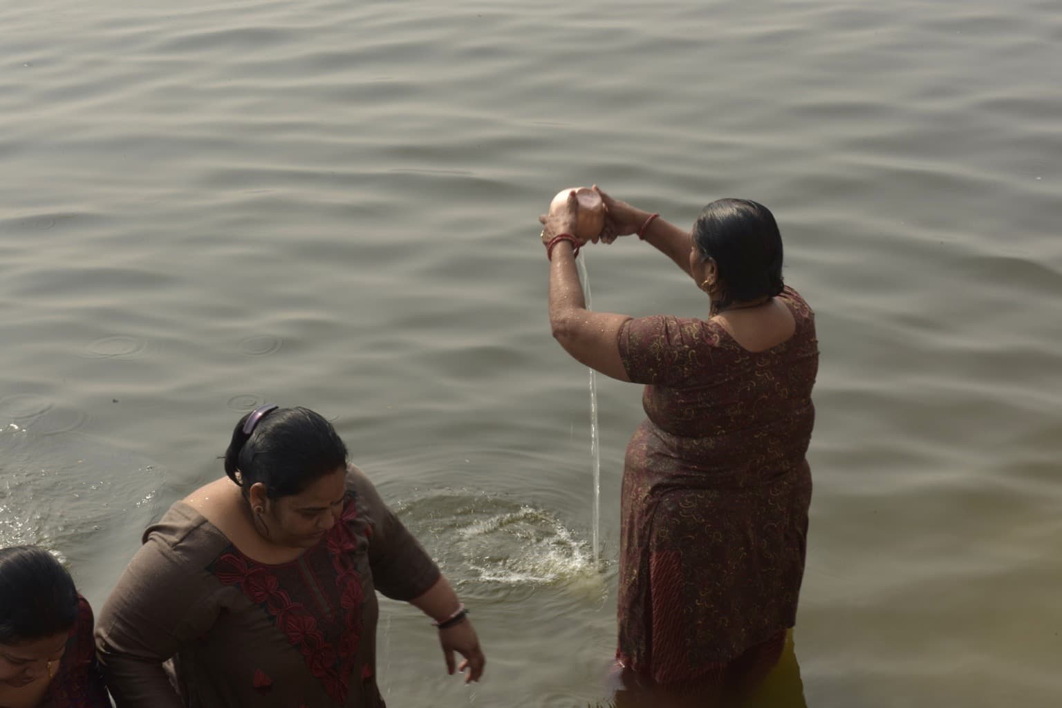 Two women bathe in the Ganges, one lifting water above her head, Varanasi, 2019