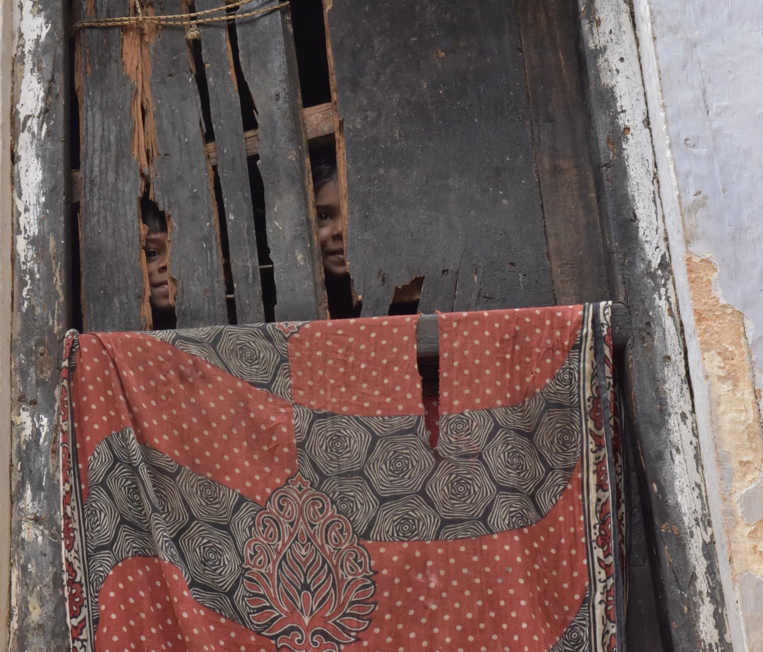 A red and grey patterned textile hangs across weathered wooden bars in Varanasi, 2019