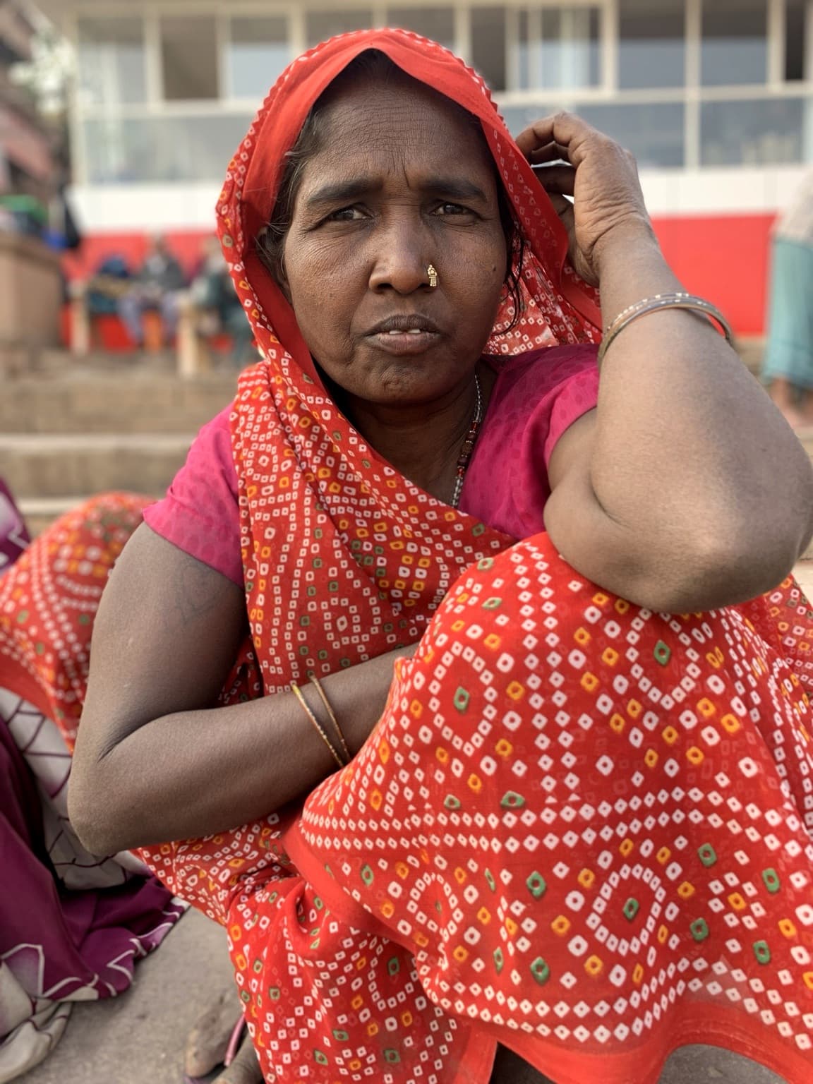 A mature woman is photographed directly on the ghats, with colour and gesture carrying the portrait, Varanasi, 2019.