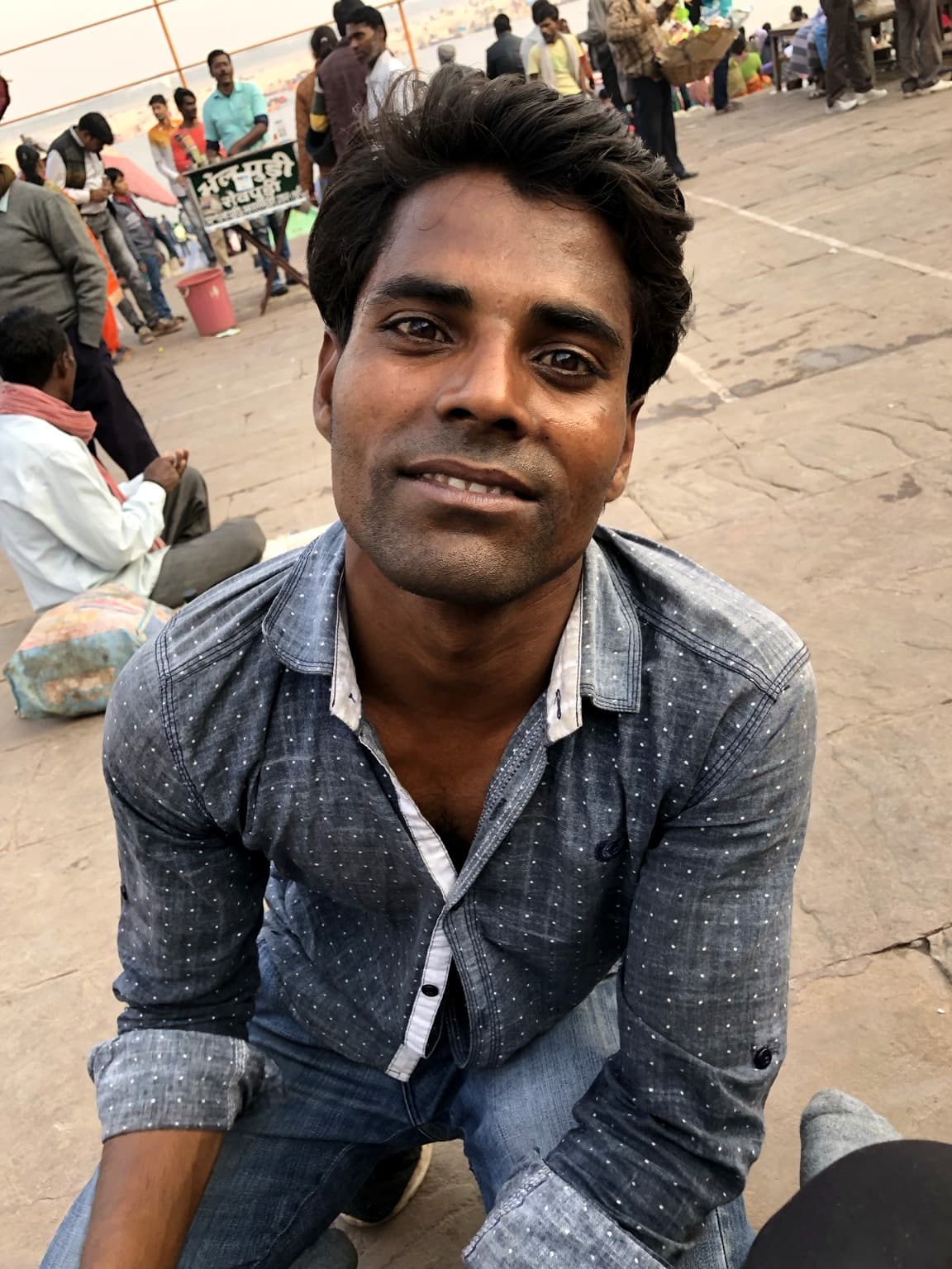 A young man seated on the stone ghats looks directly into the camera, Varanasi, 2019.