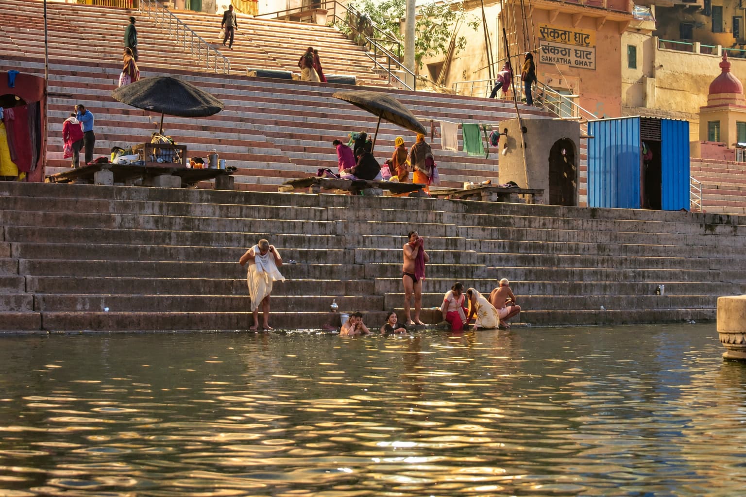 People occupy broad riverfront steps above the reflective water of the Ganges in Varanasi, 2019