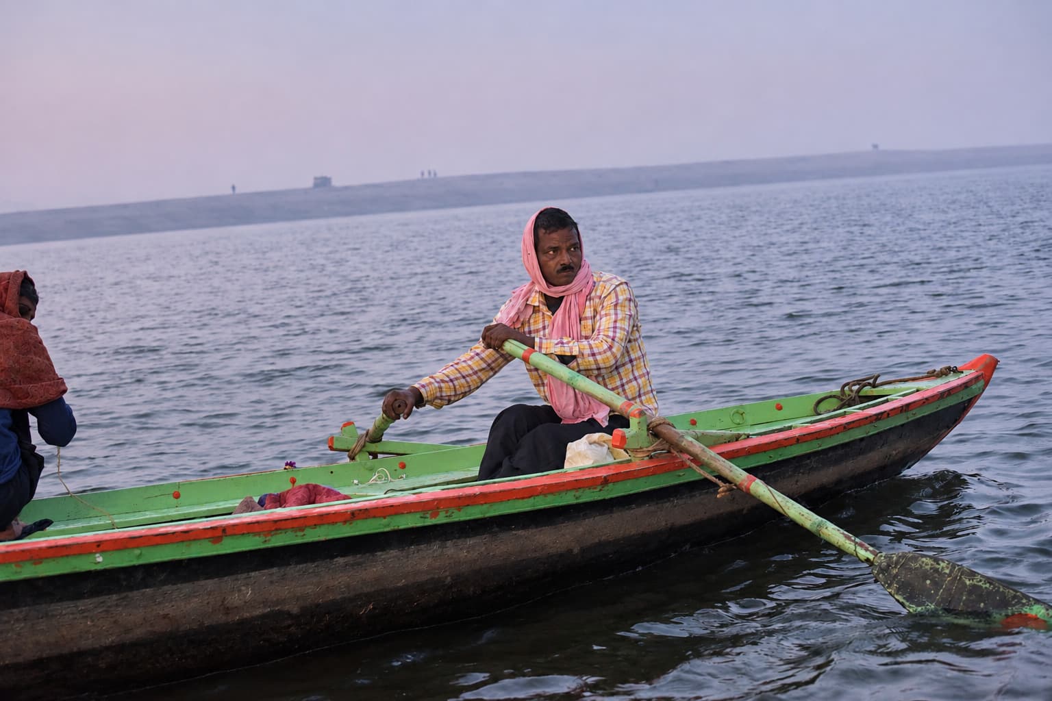 A woman rows a brightly painted green and red boat across the Ganges in Varanasi, 2019