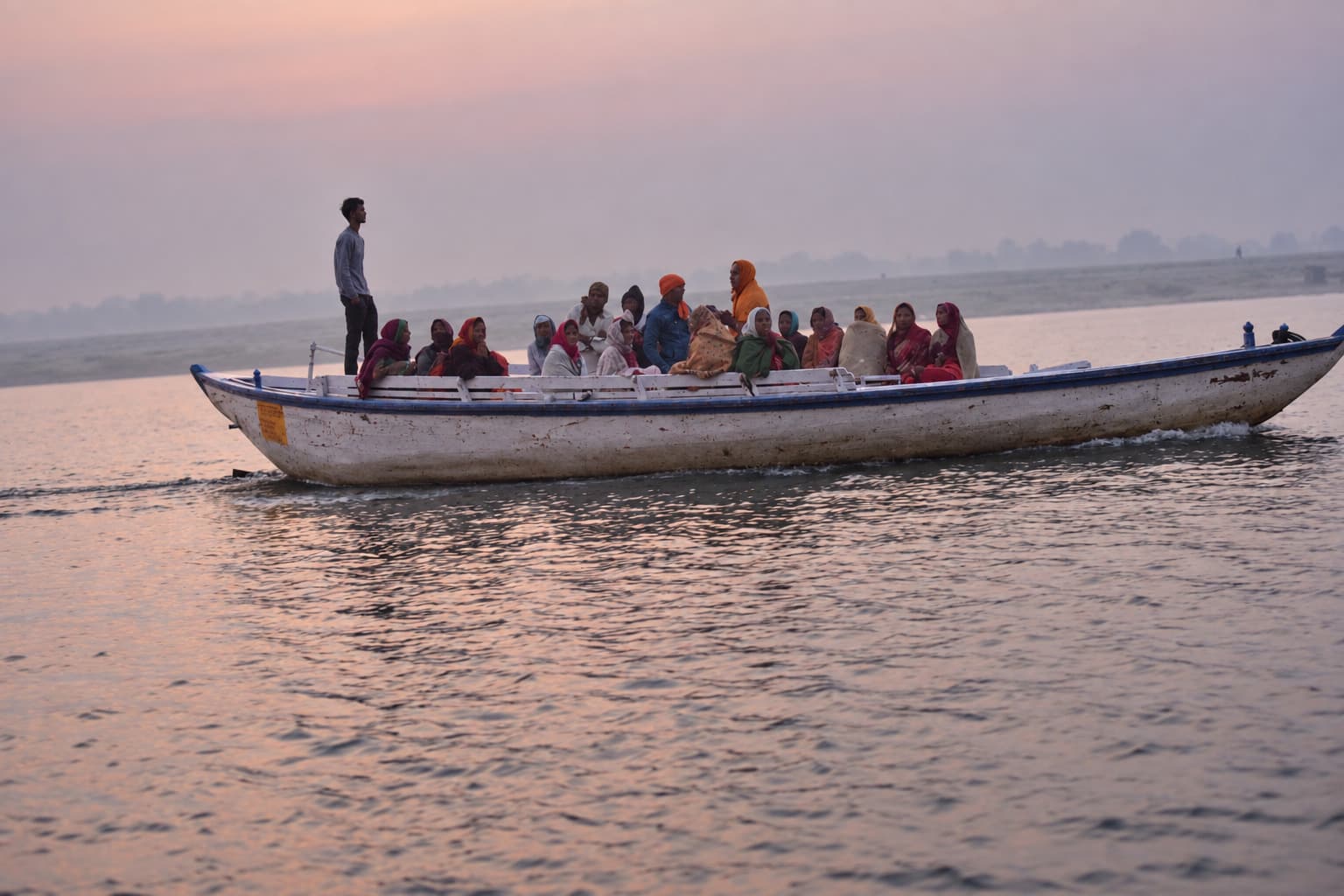 A passenger boat crosses the Ganges beneath a pale rose sky in the haze of Varanasi, 2019