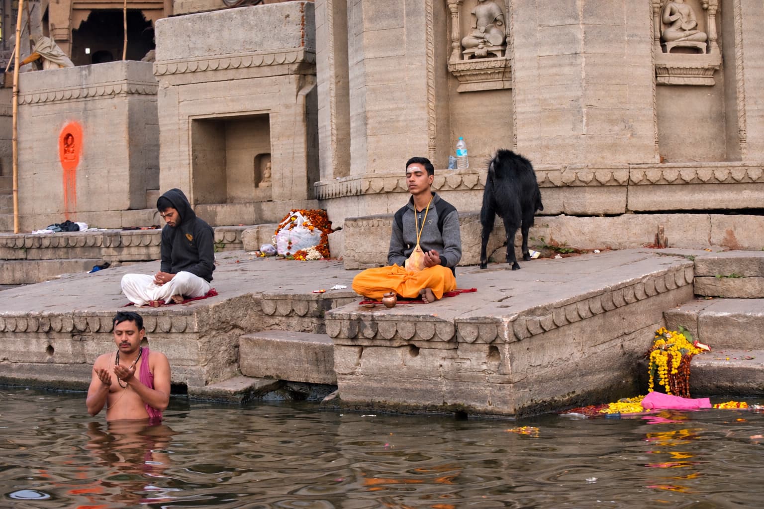 People bathe and sit on the lower ghat steps while animals and belongings occupy the riverfront behind them, Varanasi, 2019