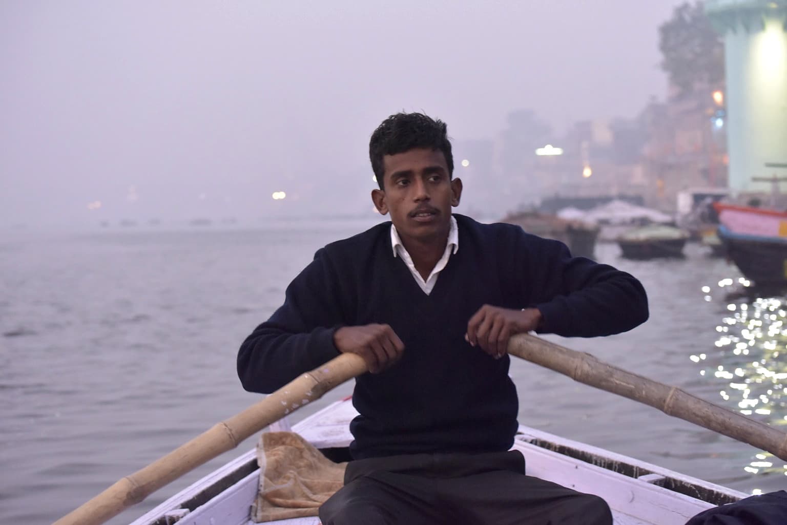 A young boatman rows directly toward the camera through the morning haze on the Ganges in Varanasi, 2019