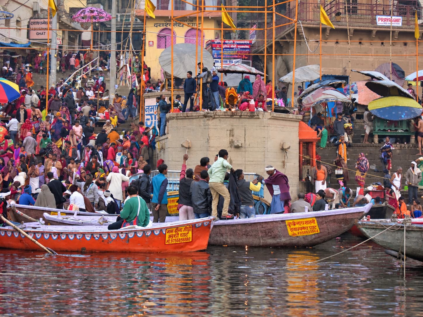 Crowded ghat steps and several working boats fill the frame at the edge of the Ganges in Varanasi, 2019