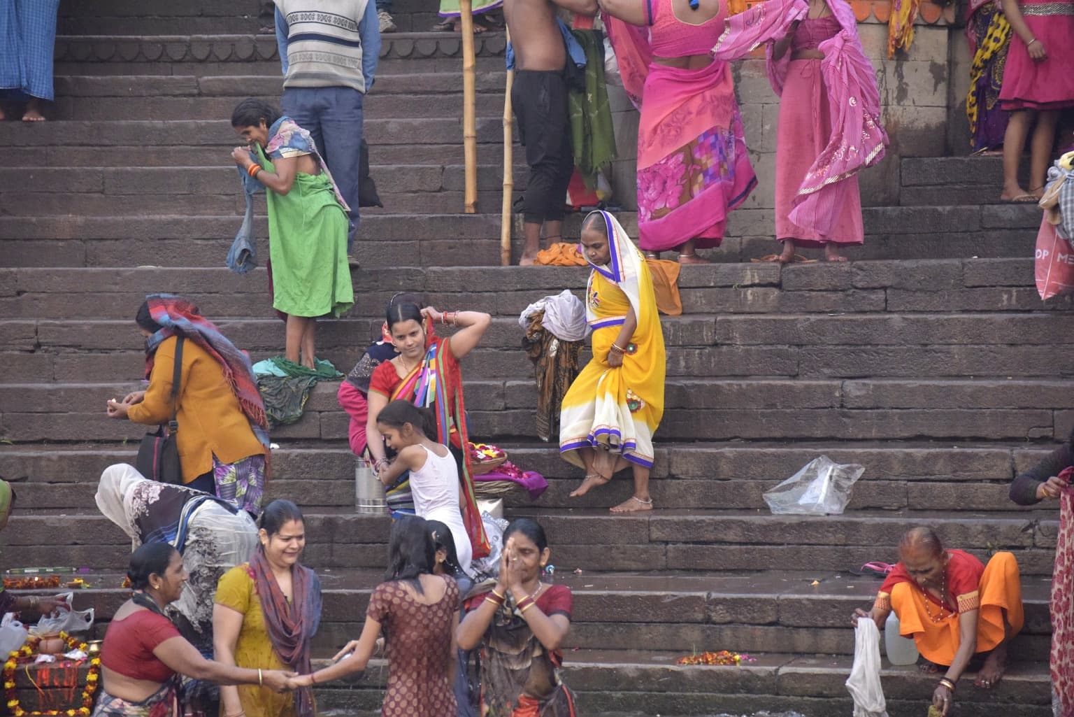Women in vivid green, yellow, pink and red clothing dress, prepare and gather on the ghat steps in Varanasi, 2019