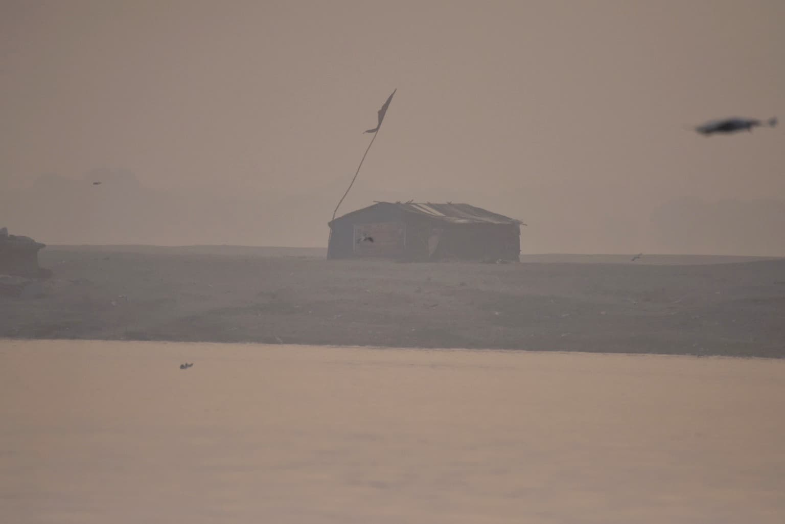 A small riverside shelter stands alone on the hazy far bank of the Ganges in Varanasi, 2019