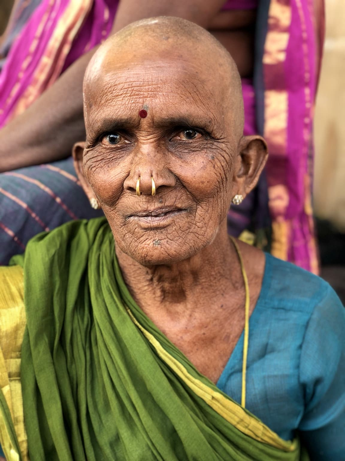 An elderly woman in a green sari and blue blouse is photographed closely in Varanasi, 2019