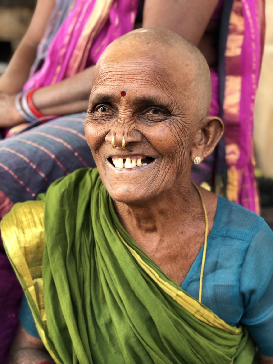 An elderly woman in a green sari looks upward with a broad smile during a close portrait in Varanasi, 2019