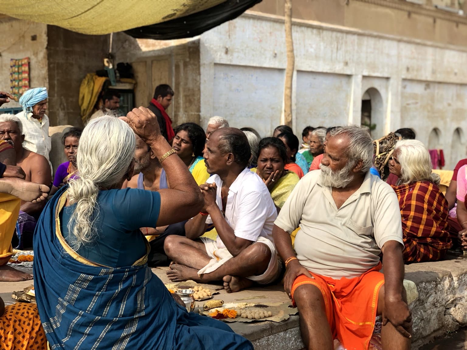 A dense group of people sits and gathers around ritual objects on the ghats of Varanasi, 2019