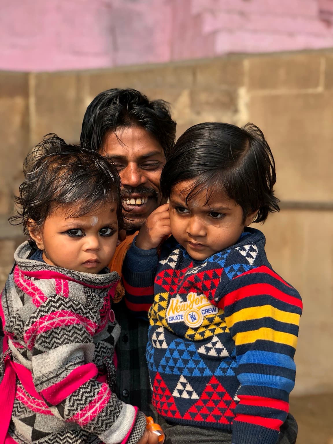 A smiling father holds two young children close for a warm family portrait in Varanasi, 2019