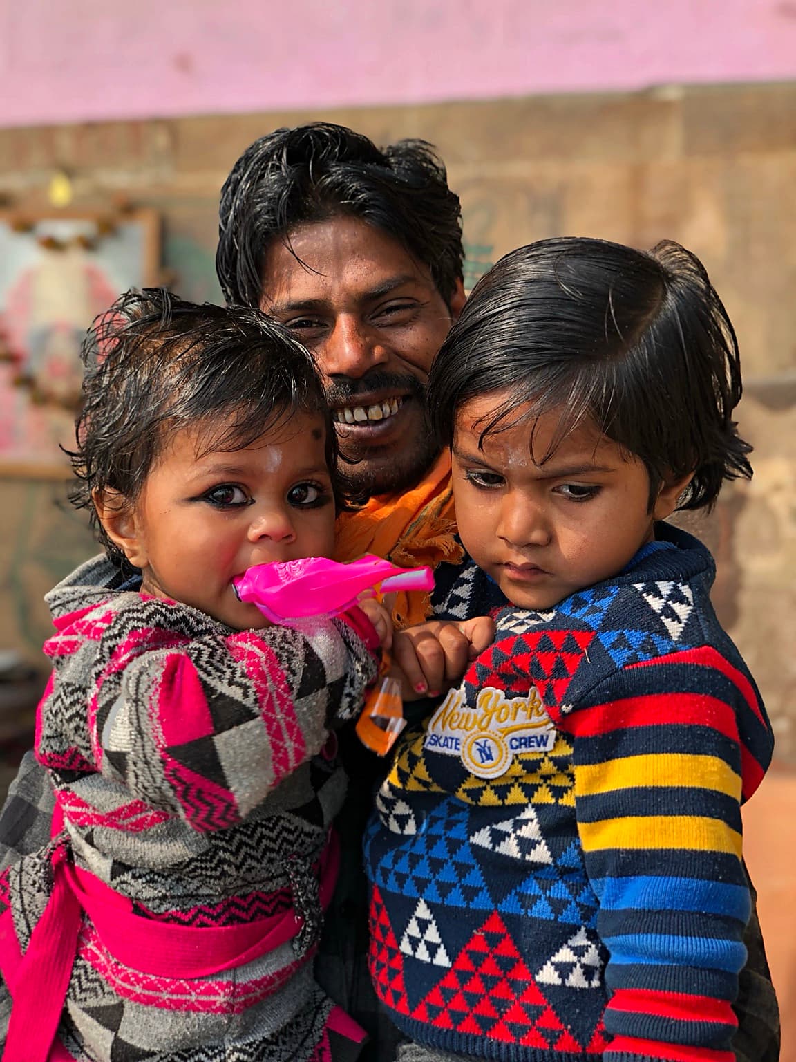 A smiling father holds two young children close on the ghats of Varanasi, 2019