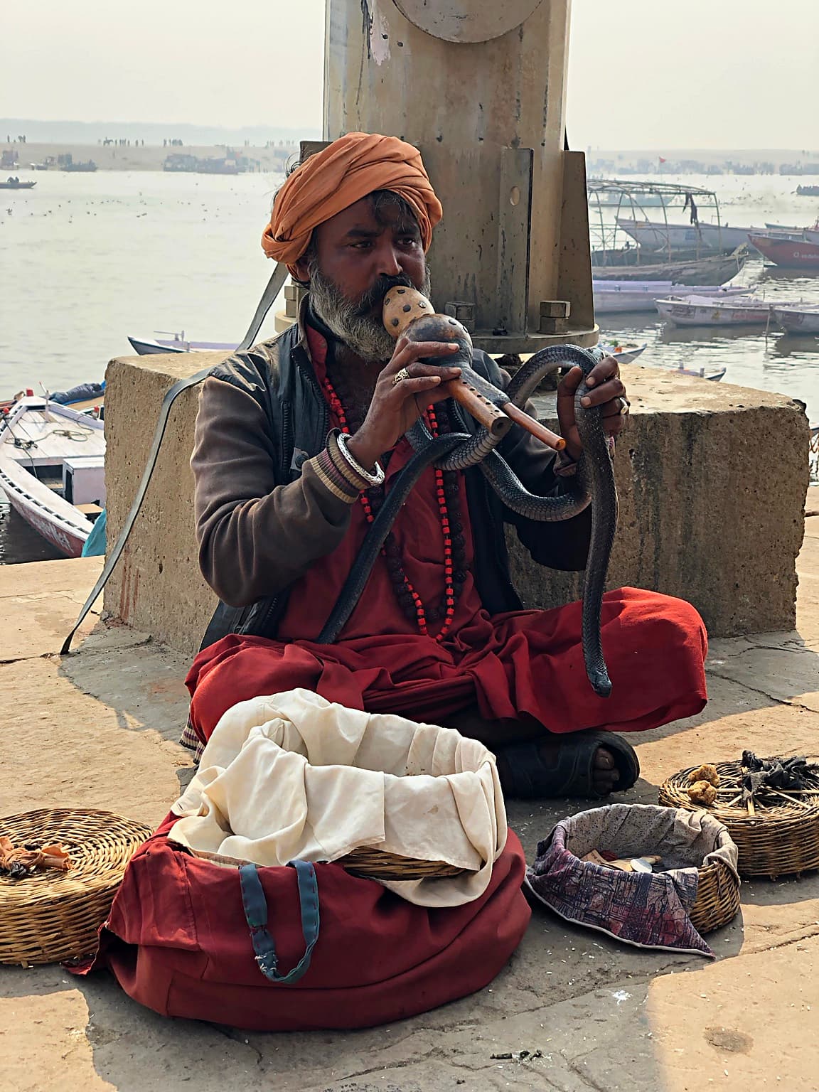A snake charmer plays a pungi while a cobra rises from an open basket on the ghats of Varanasi, 2019