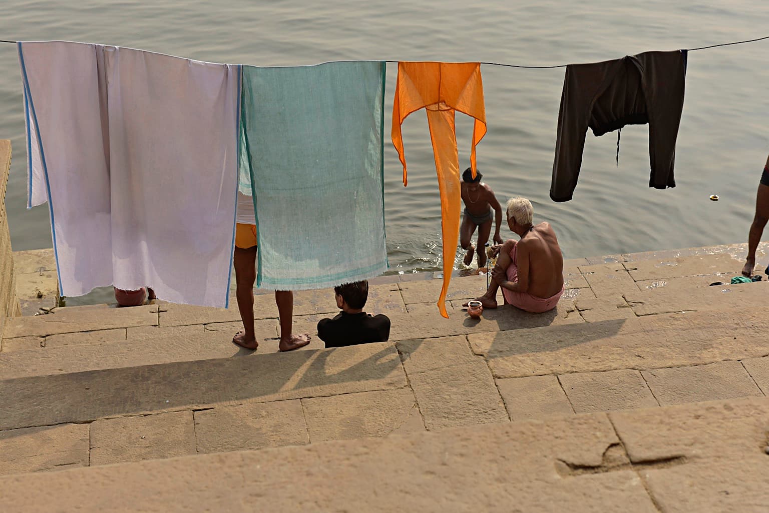 Hanging laundry fills the foreground while daily life on the riverbank is glimpsed through and beyond it in Varanasi, 2019
