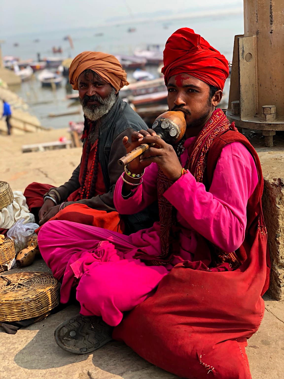 A woman in a vivid purple sari moves beside the Ganges with boats and bathers beyond her in Varanasi, 2019