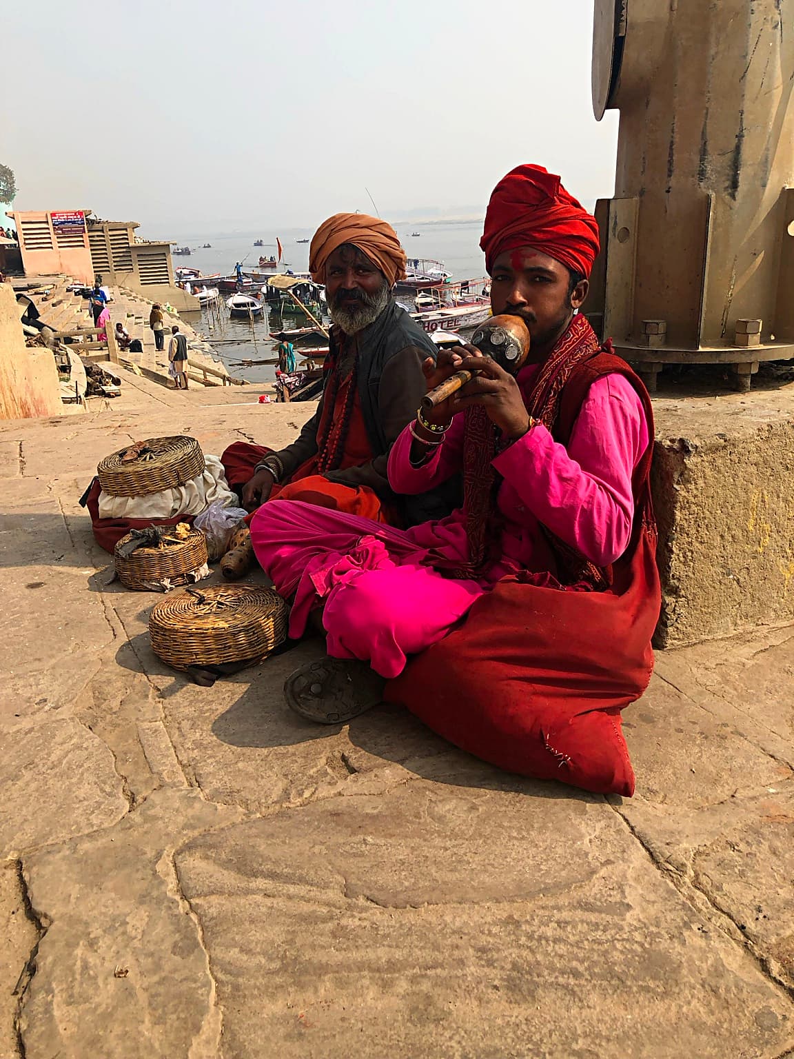 A musician plays a pungi beside an open basket as a cobra rises before him on the ghats of Varanasi, 2019