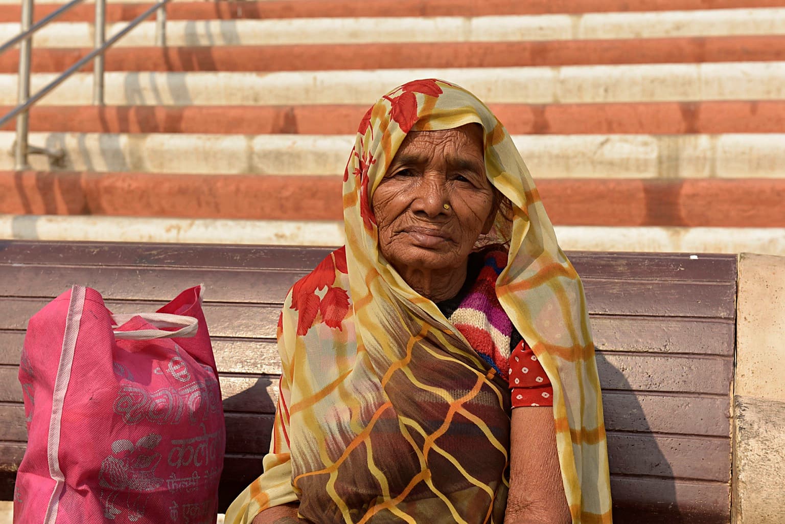 An older woman sits quietly on a bench along the ghats of Varanasi, 2019