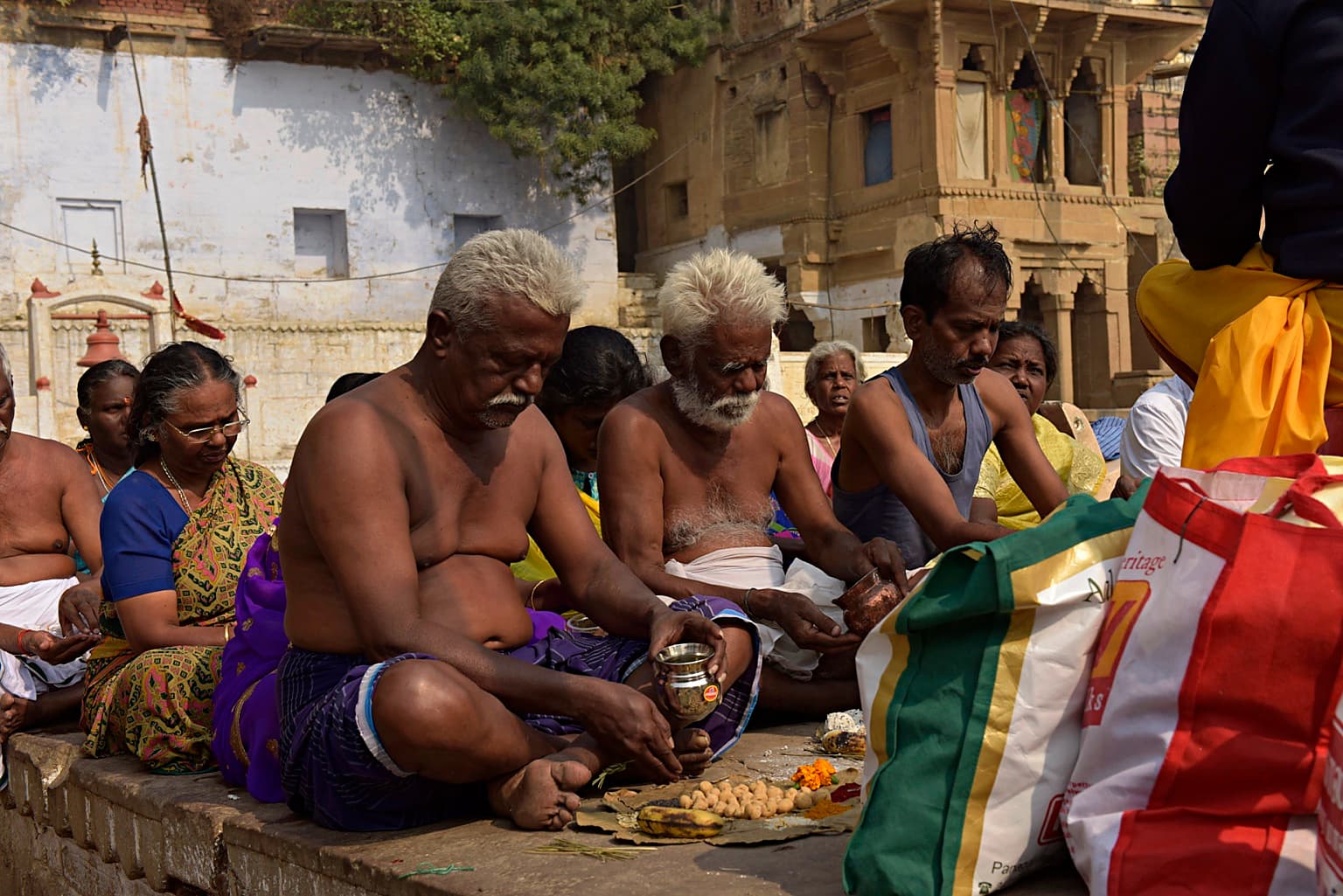 Men work closely around vessels and offerings during a ritual gathering on the ghats of Varanasi, 2019