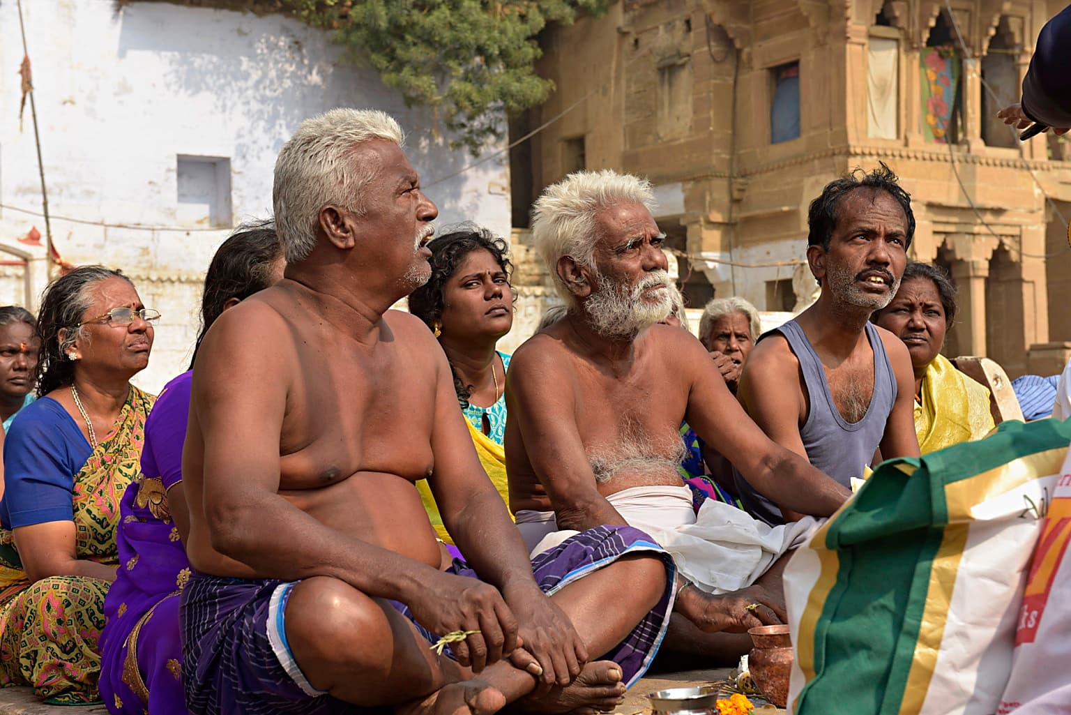 A close group at a ritual gathering looks upward amid the activity of the ghats in Varanasi, 2019
