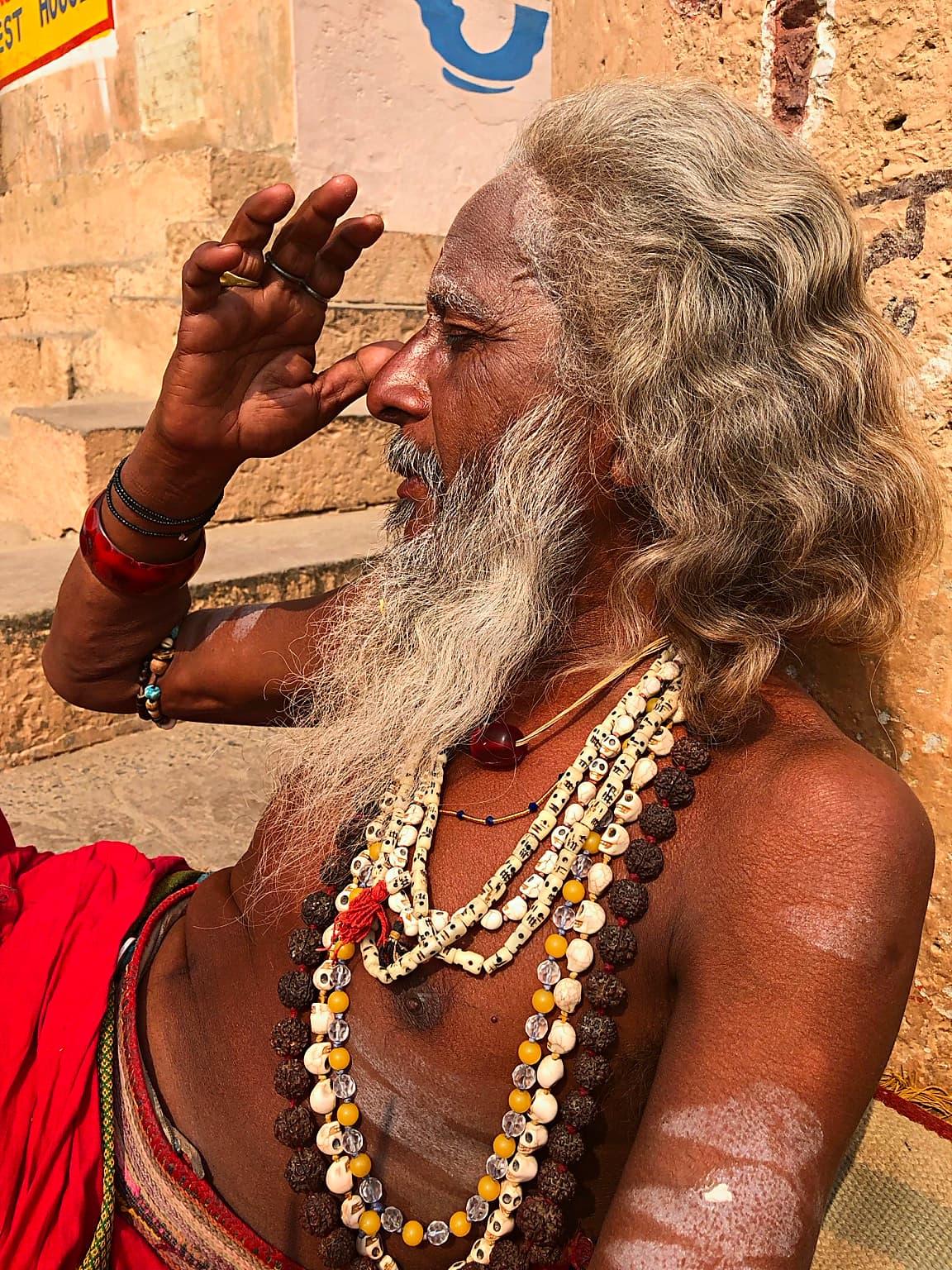 A long-haired sadhu is seen in profile with one hand raised near his face in Varanasi, 2019