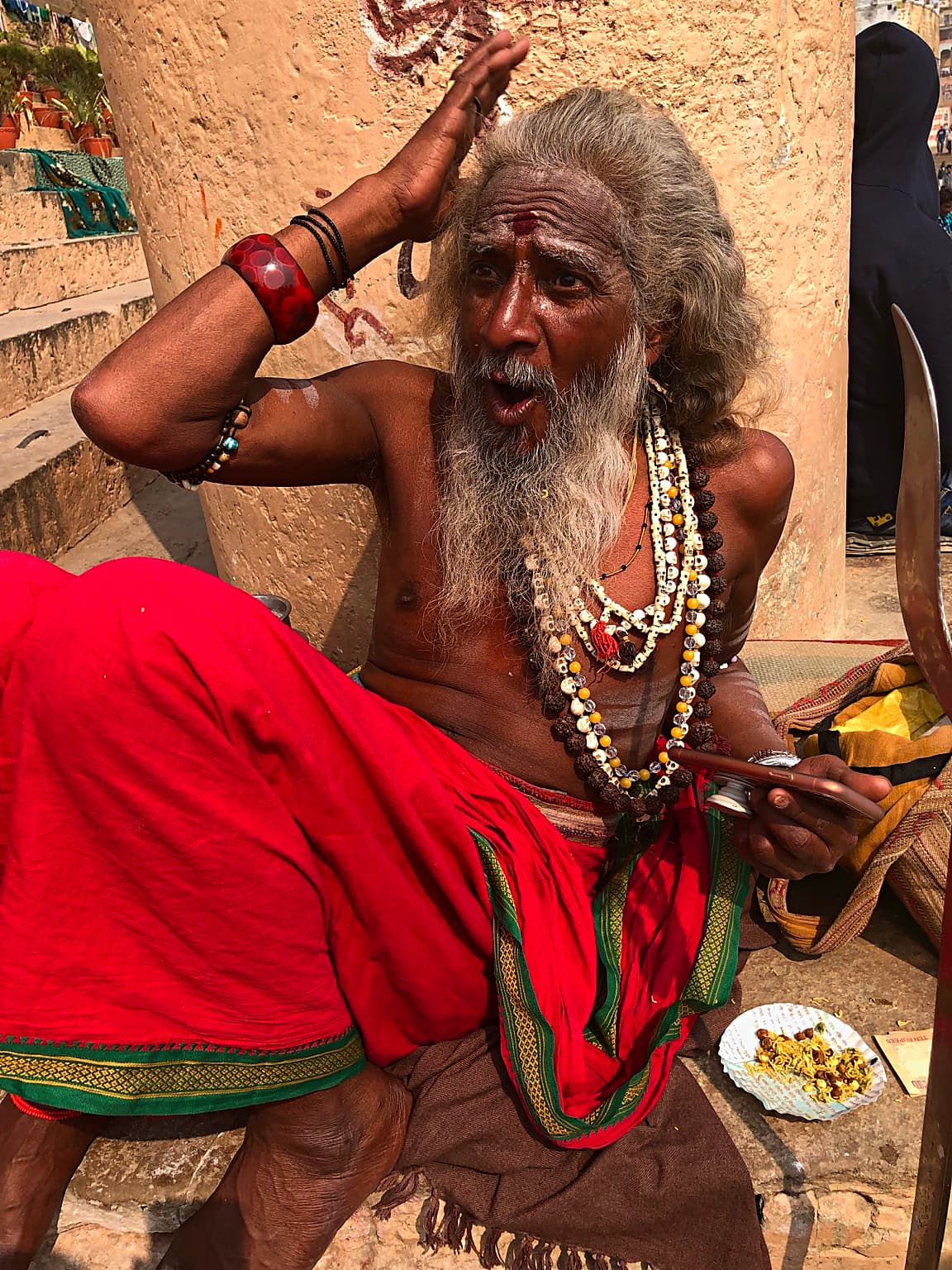 A seated sadhu touches his head while speaking or reacting during an encounter on the ghats of Varanasi, 2019