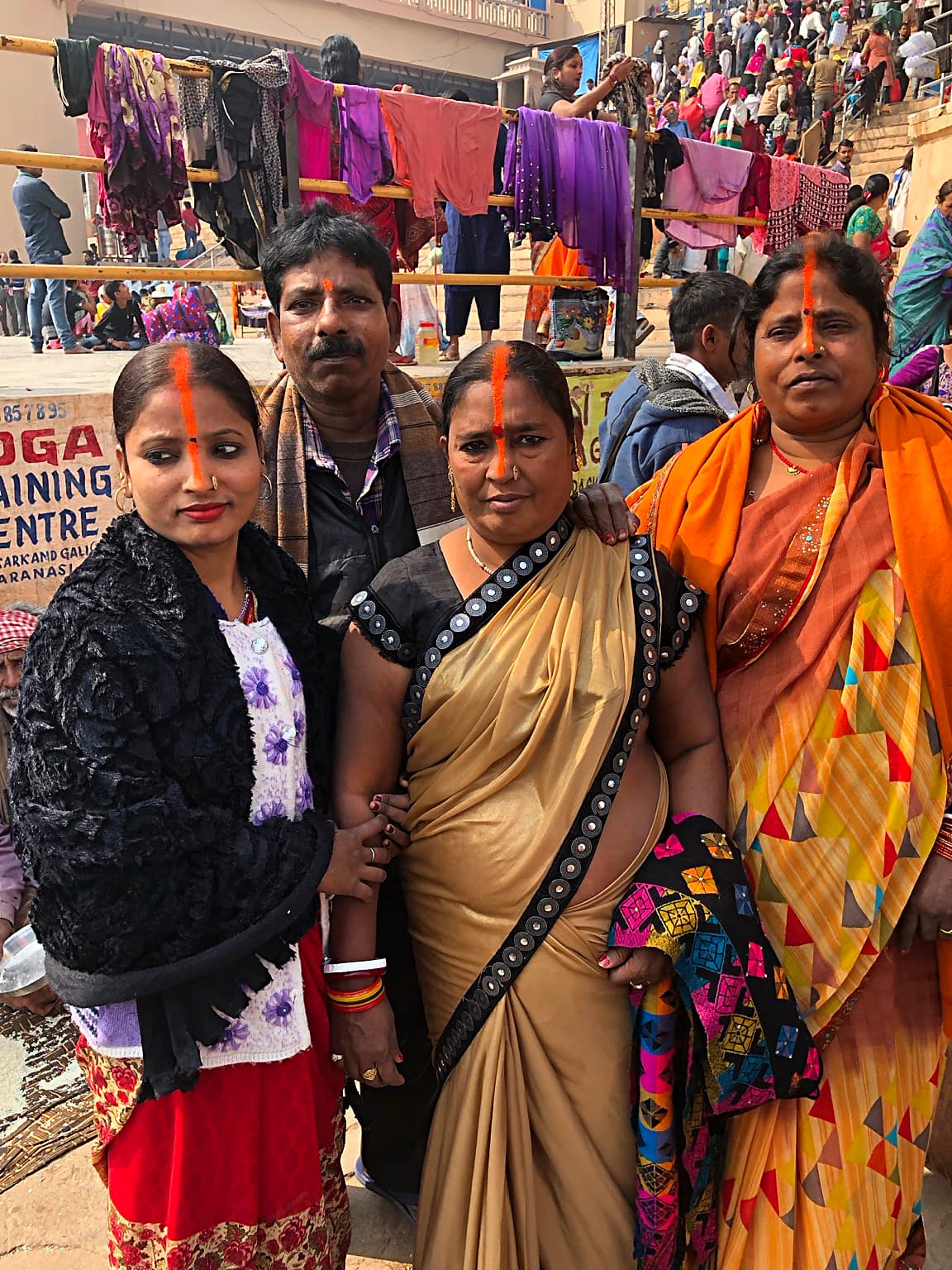 Three women and a man stand together for a close group portrait amid the busy ghats of Varanasi, 2019