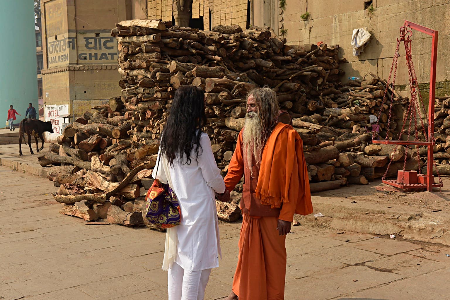 Two people face one another closely before a large stack of firewood at Jalasen Ghat in Varanasi, 2019