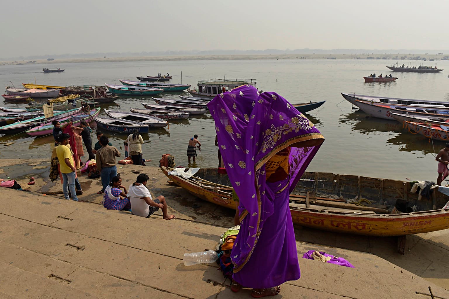 A woman in a vivid purple sari adjusts her clothing on the ghat steps above the Ganges in Varanasi, 2019
