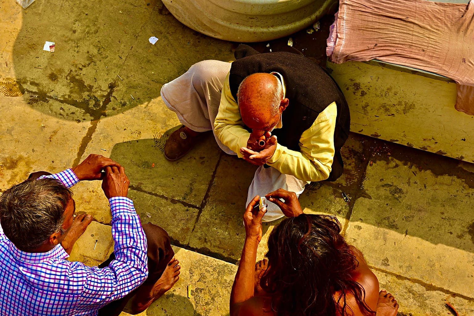 Three men are seen from above during a small gathering on the ghats of Varanasi, 2019