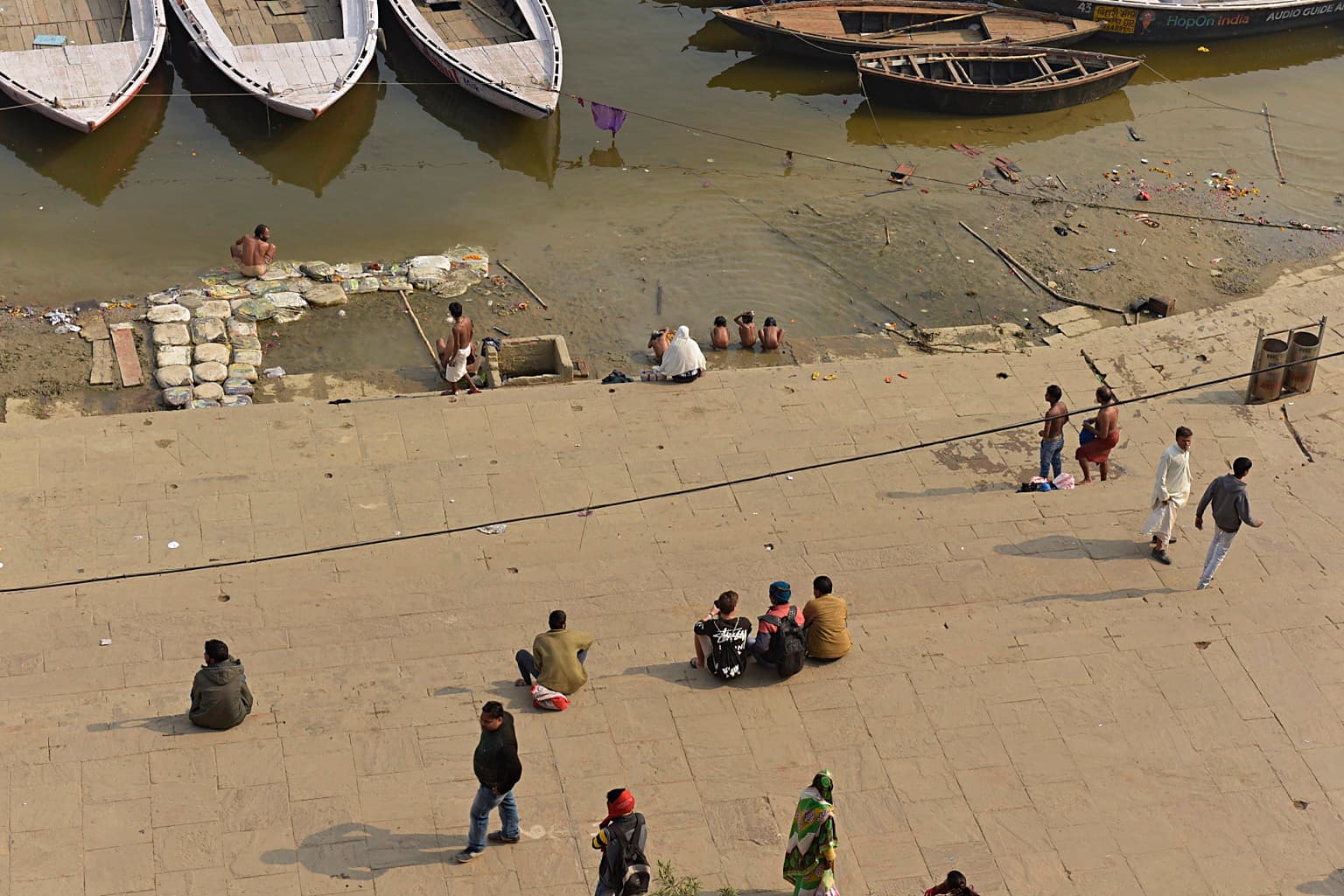 A high view looks down over people scattered across broad ghat steps toward boats at the Ganges in Varanasi, 2019