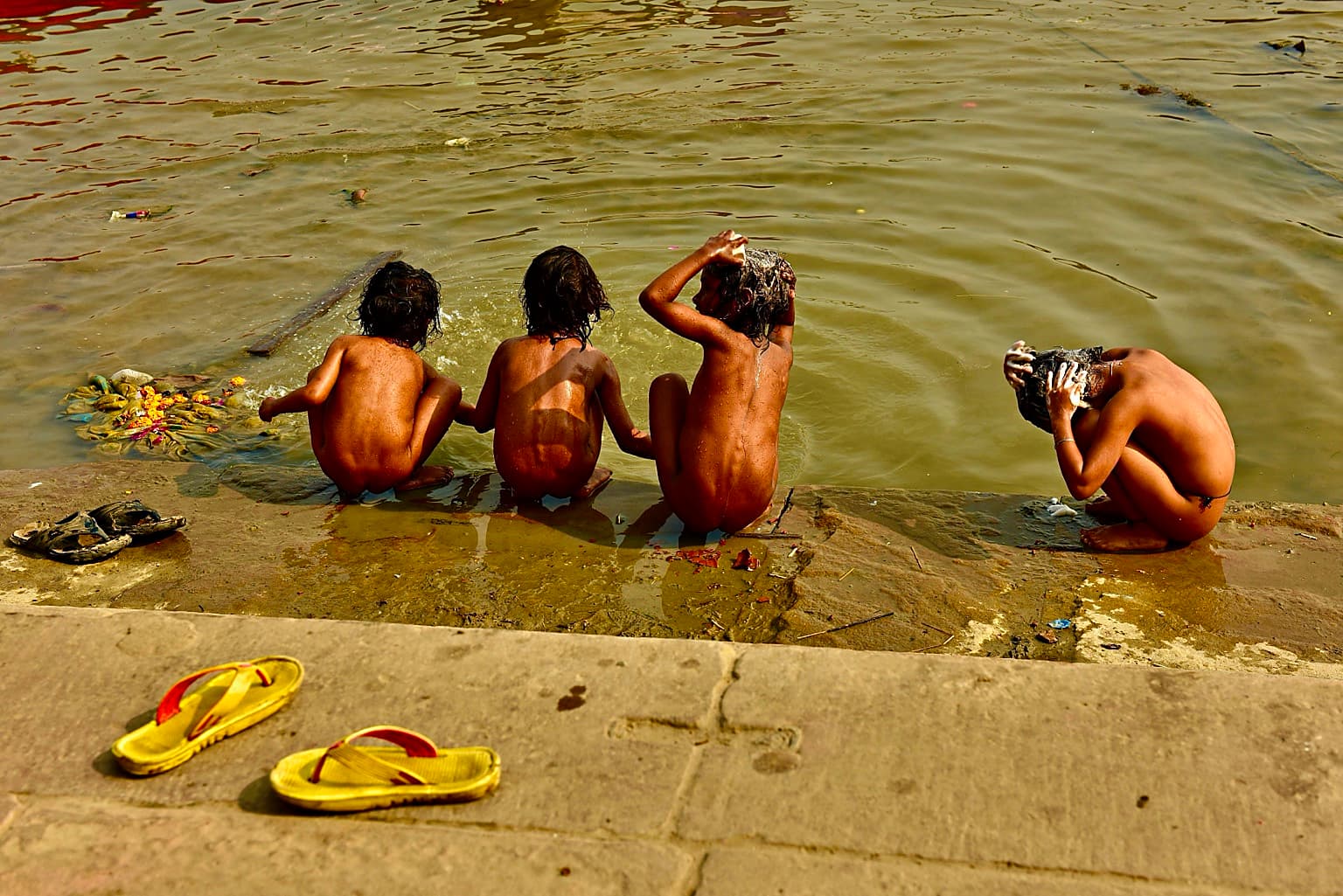 Four children wash their hair and bathe together at the edge of the Ganges in Varanasi, 2019