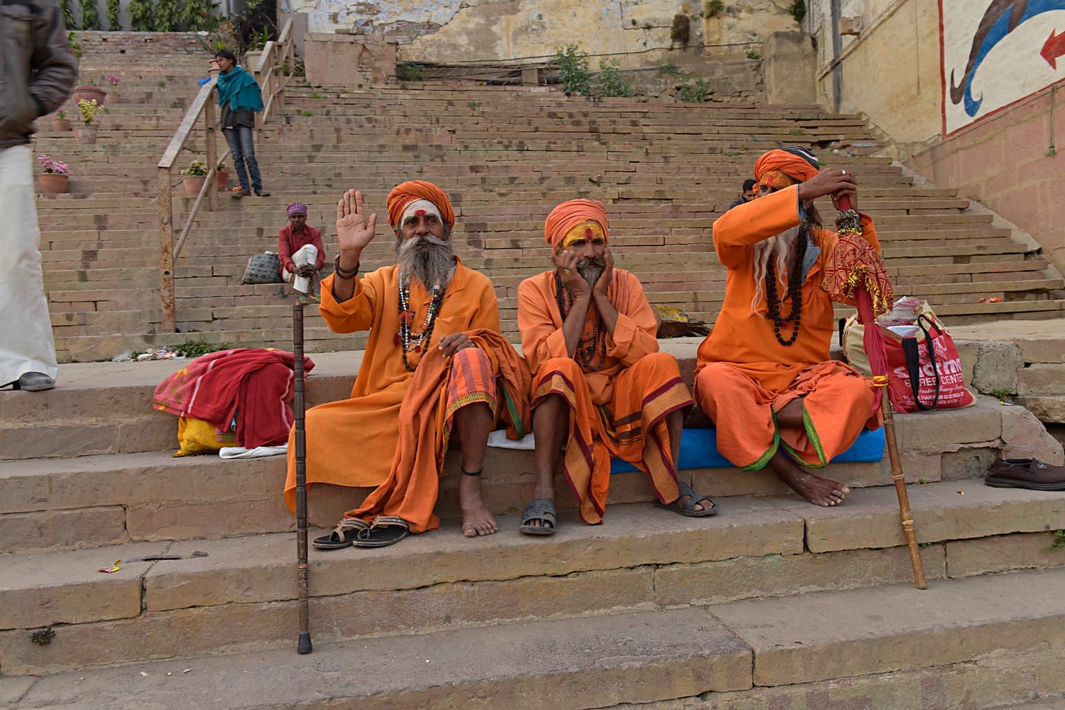 Three sadhus in orange robes sit together on broad stone steps in Varanasi, 2019