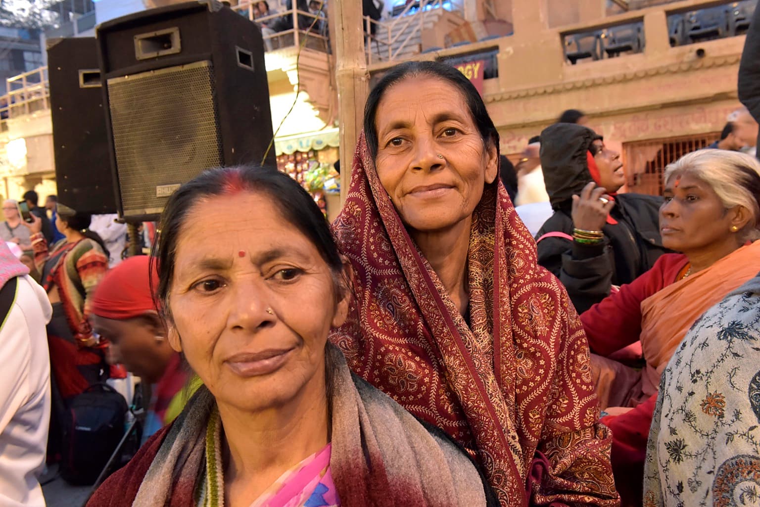 Two women stand close together for a portrait amid a crowded riverside gathering in Varanasi, 2019
