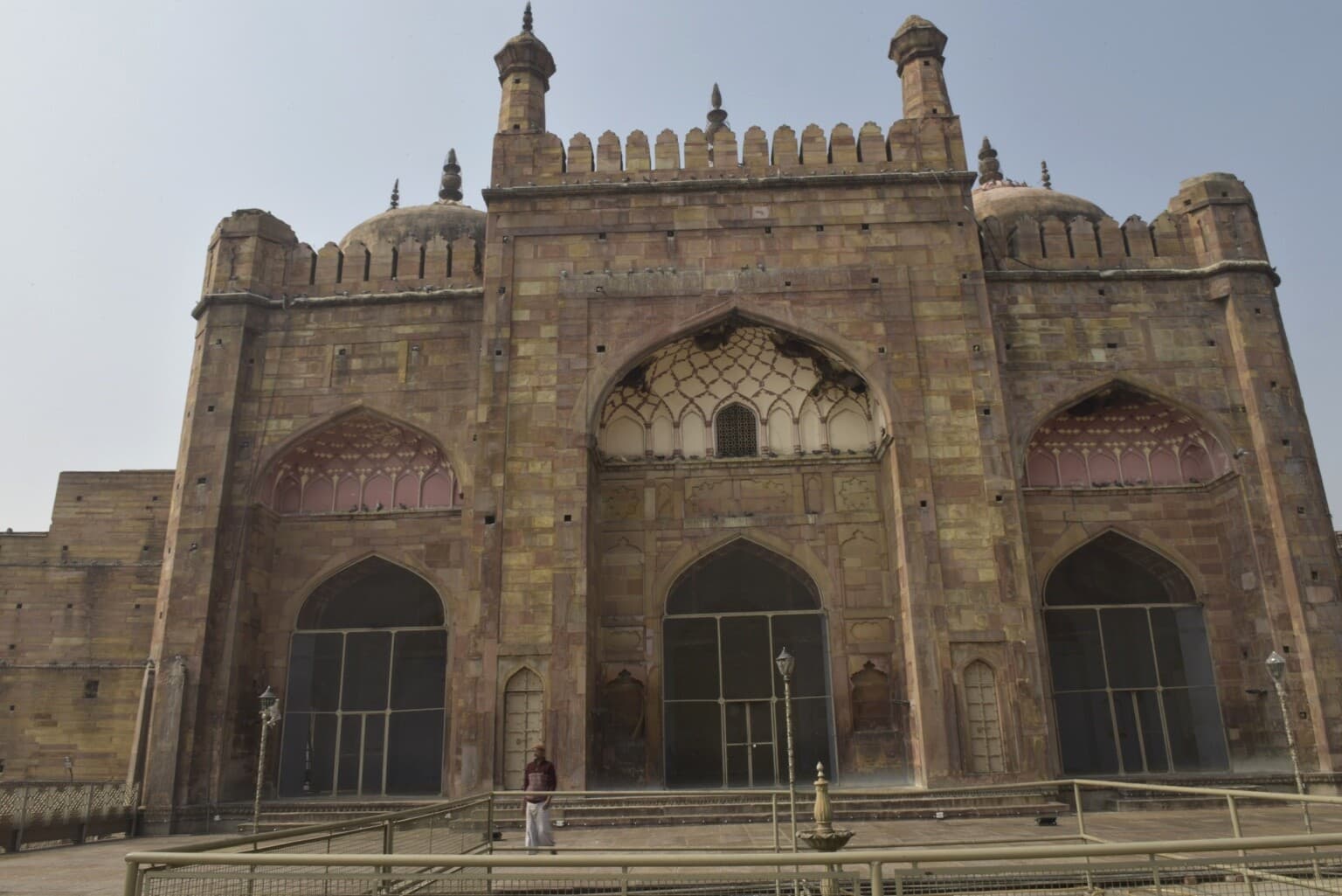 The broad sandstone façade of a riverfront mosque rises above a solitary figure in its courtyard in Varanasi, 2019