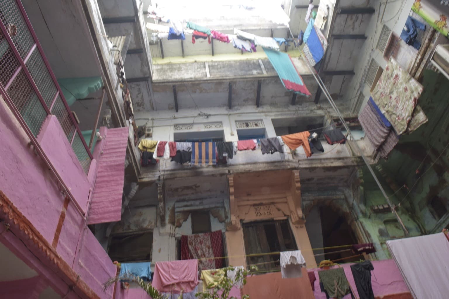 A multi-storey residential courtyard rises around lines of drying laundry, with pink, green and weathered walls in Varanasi, 2019