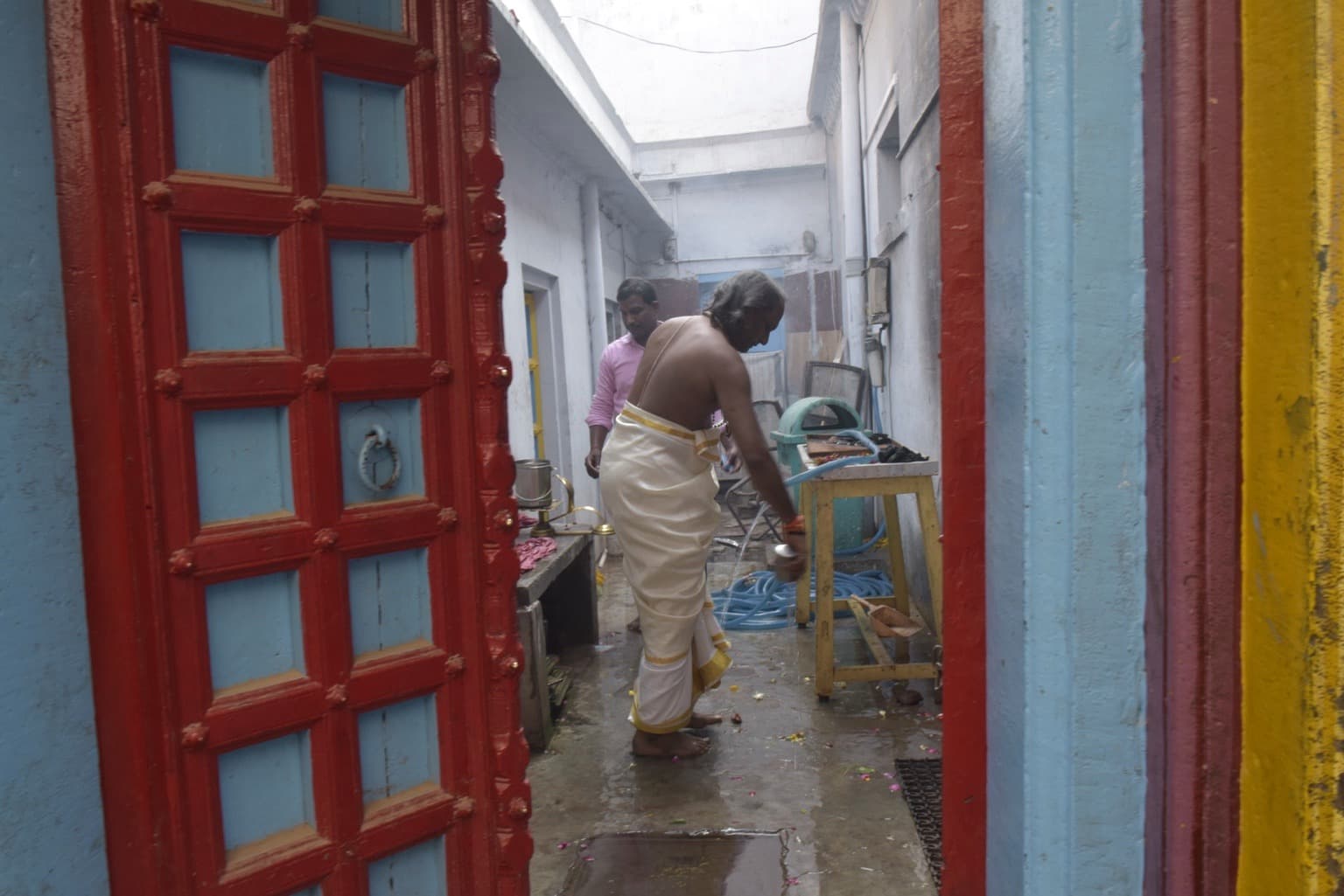Two men work inside a narrow service area framed by vivid red, blue and yellow painted doorways in Varanasi, 2019