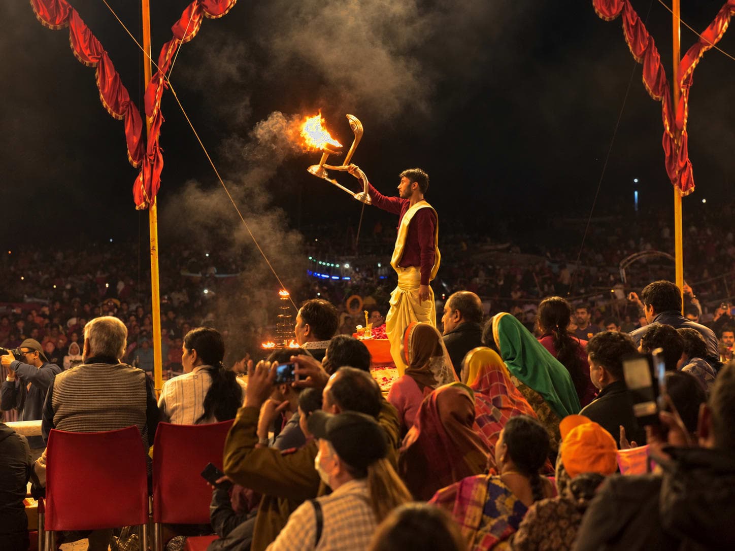A priest extends a large flaming lamp before the crowd during evening Ganga aarti in Varanasi, 2019