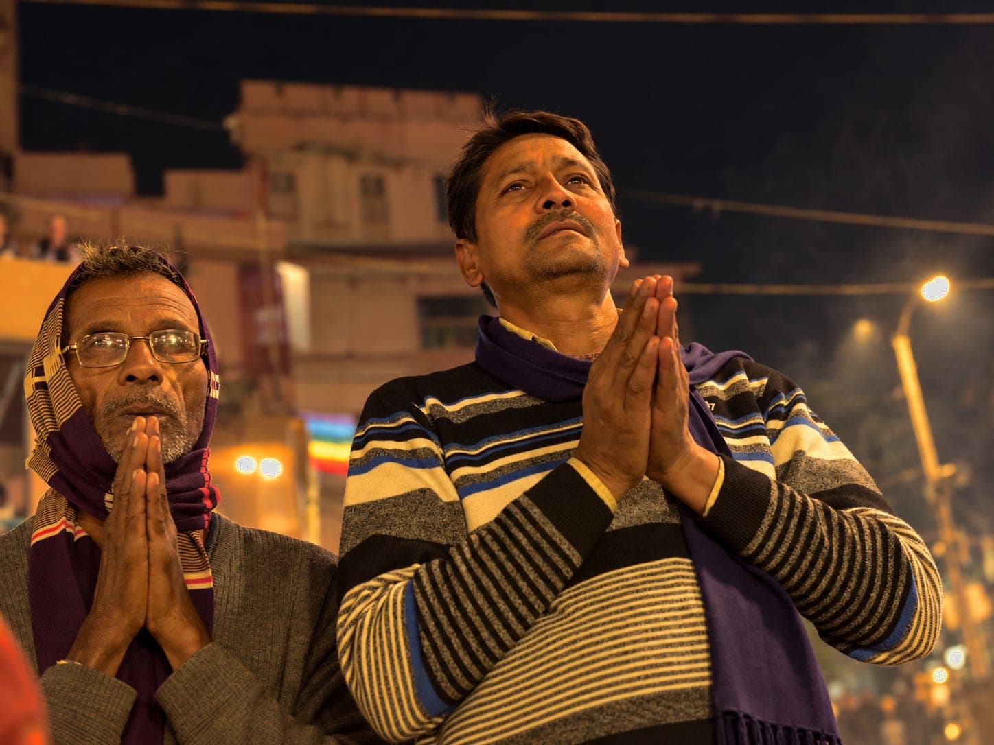 Two men stand close together with palms pressed in prayer during the night ceremony in Varanasi, 2019