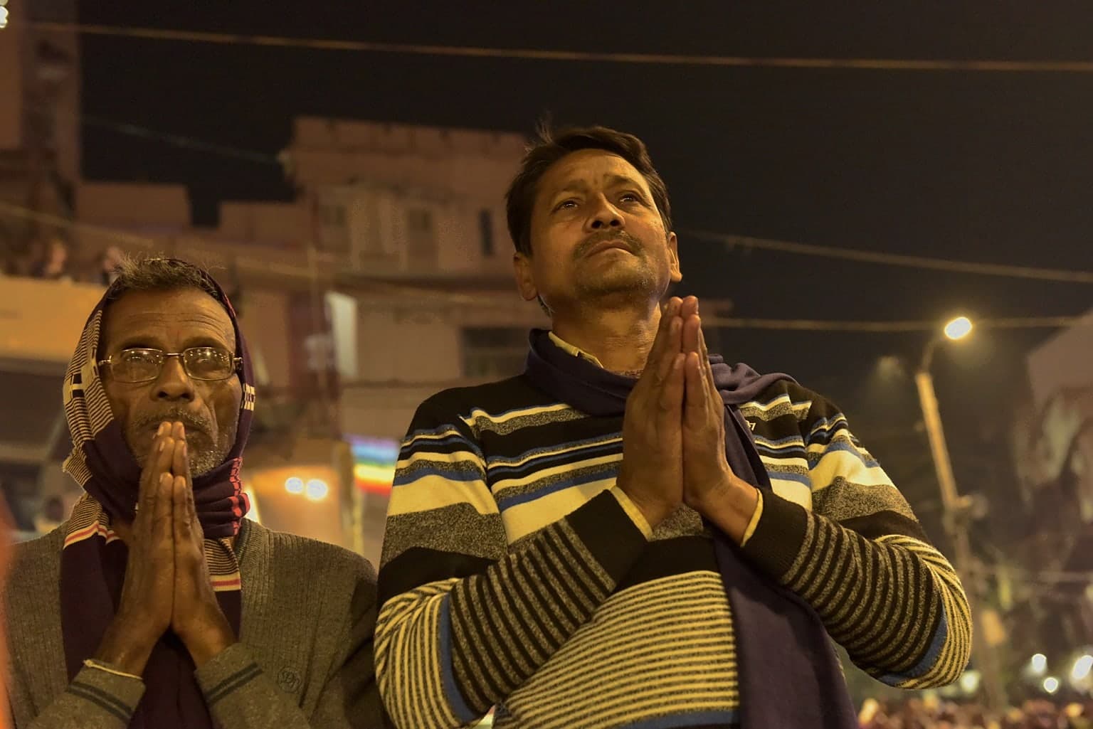 Two men stand with palms pressed together in prayer during the evening gathering in Varanasi, 2019