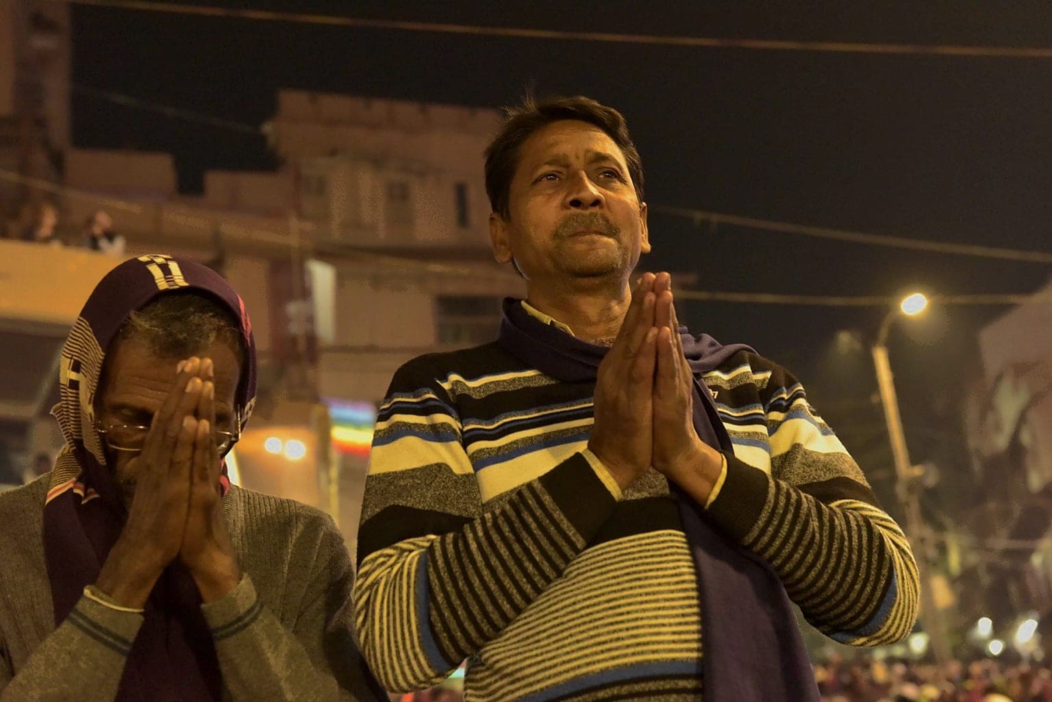 Two men pray side by side beneath warm night lighting in Varanasi, 2019