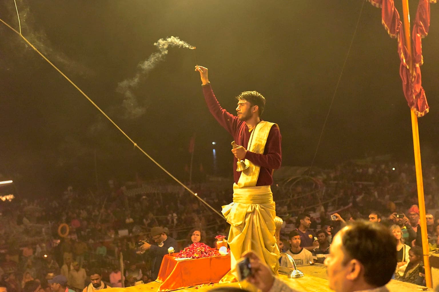 A priest raises a smoking incense vessel during evening Ganga aarti before a large crowd in Varanasi, 2019