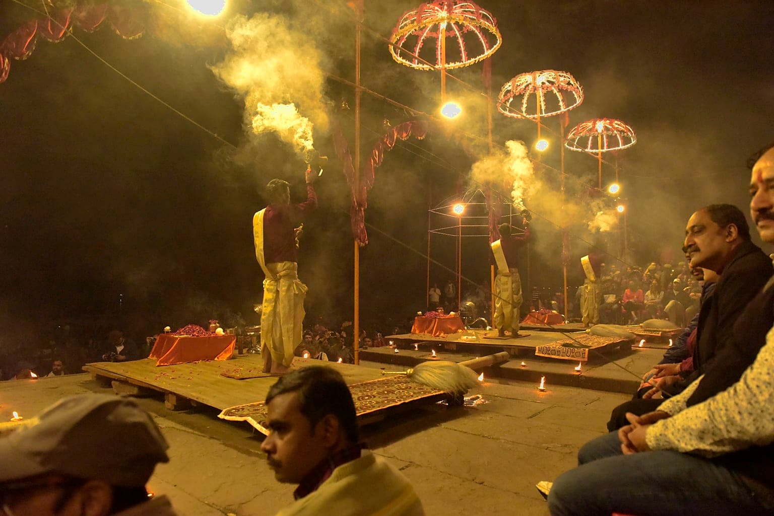 Priests perform evening Ganga aarti across several platforms as smoke hangs above a dense audience in Varanasi, 2019